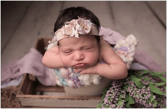 beautiful baby girl surrounded by flowers and wearing flower crown for photo shoot during newborn photo shoot